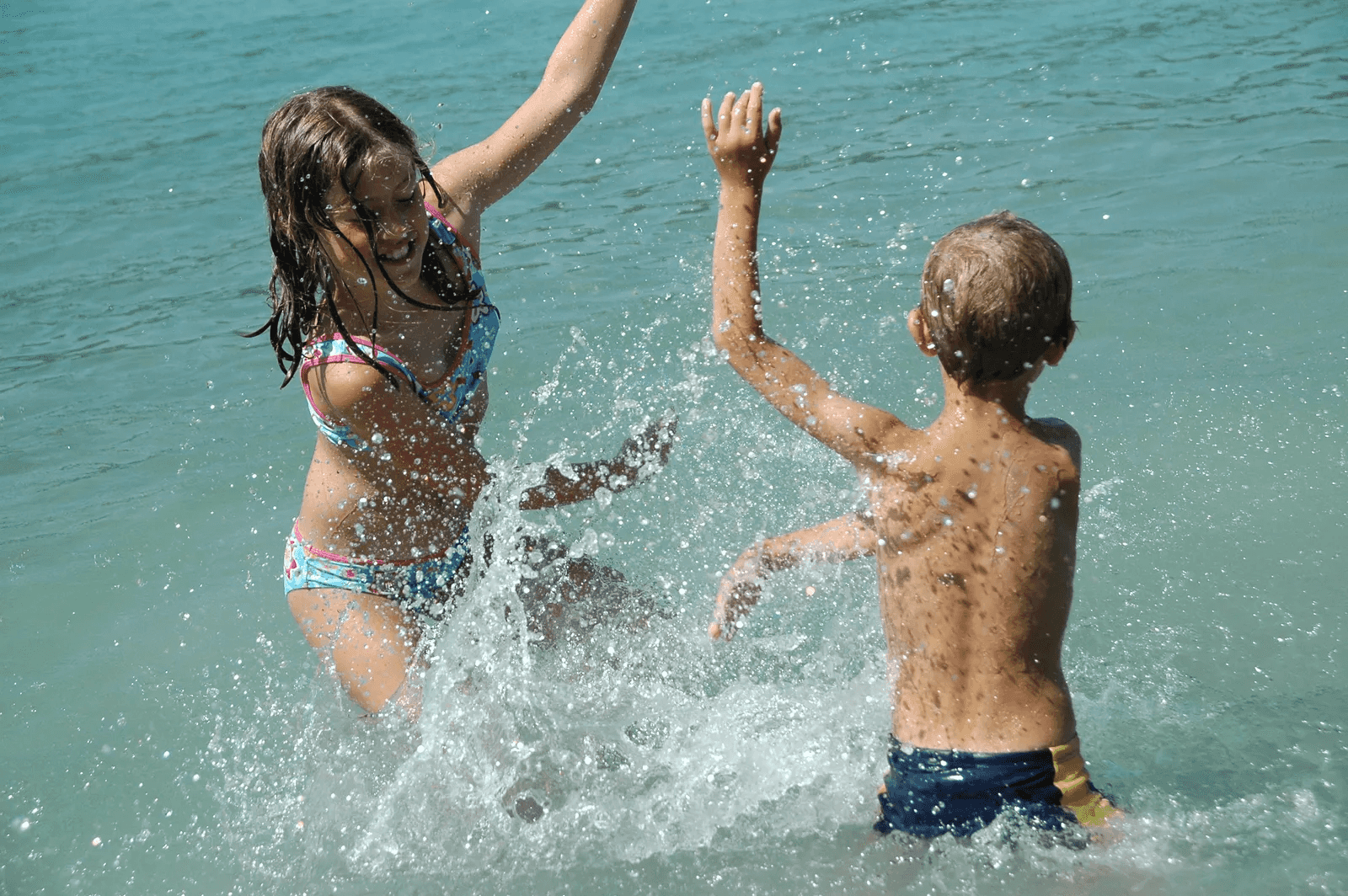 Zwei Kinder spritzen sich im flachen Wasser gegenseitig nass